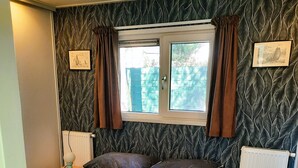 A bedroom with a bed, a window with curtains, a bedside table with a lamp, and a radiator. - Luxury, space, comfort and nature for two: The Veluwe Happy Together! (Epe)