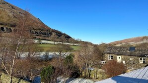 A stone building with a sloped roof, a clear sky, and a valley with sparse vegetation.