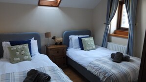A bedroom with two beds, a nightstand, a lamp, and a window with curtains.