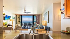 A modern kitchen with a large island, a dining area with a view, and a living room with a sofa and chairs.