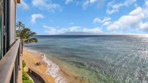 A beach view from a balcony overlooking a sandy shore with clear water and a palm tree. - MK404 - Sleep at the Ocean and Watch Sunsets 3-Bed Suite (Lahaina)
