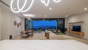 A modern living room with a large marble table, a dining area with wooden chairs, a sofa, and a TV on a wooden stand.