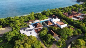 An aerial view of a coastal property with multiple buildings, a swimming pool, and lush greenery.