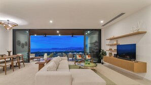 A modern living room with a large sofa, dining table, chairs, and a TV.