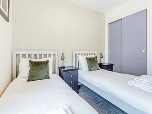 Een hotelkamer met twee bedden, elk met een nachtkastje en lamp, een grote kledingkast en een vloerbedekking.