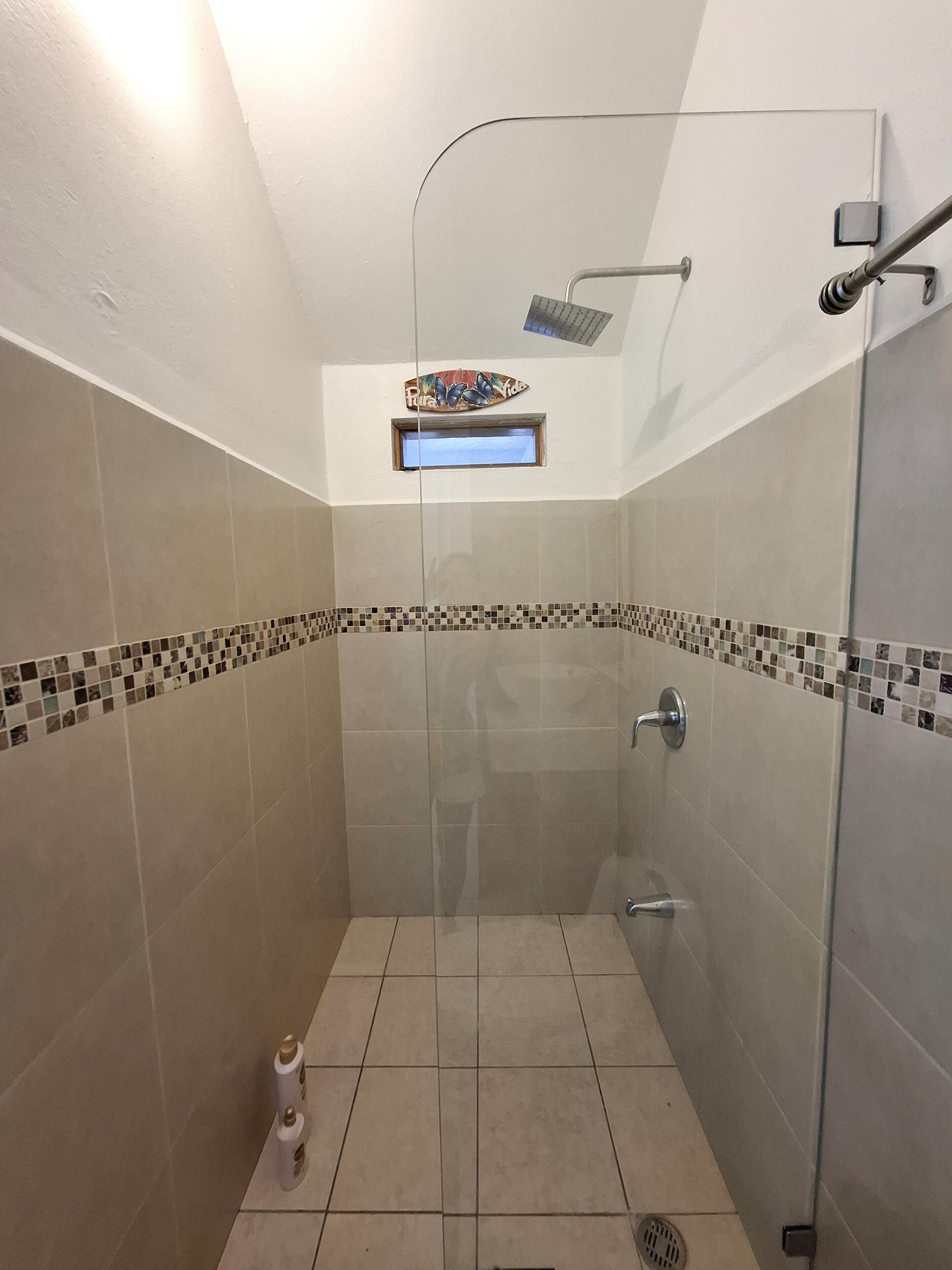 A glass-enclosed shower with a handheld showerhead, a small window, and a tiled floor with a decorative border.