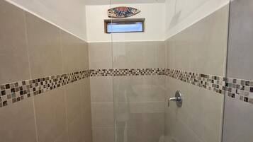A glass-enclosed shower with a handheld showerhead, a small window, and a tiled floor with a decorative border.