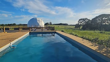 Une piscine dotée d’une terrasse en bois et, en arrière-plan, d’une structure en forme de dôme blanc.