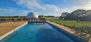 Une piscine dotée d’une terrasse en bois et, en arrière-plan, d’une structure en forme de dôme blanc.