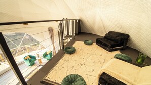 A high-ceilinged room with a view of a mountainous landscape, a black sofa, green ottomans, and a patterned rug. - Luxurious Stargazer Dome Retreat in Stunning Nature w/Hot Tub and Sauna! (Smithville)