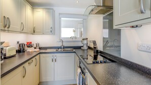 A modern kitchen with white cabinets, a black countertop, and stainless steel appliances. - 2 bedroom accommodation in Brixham (Brixham)