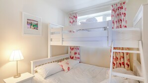 A bunk bed room with white bedding, floral curtains, a bedside lamp, and a framed picture on the wall. - 2 bedroom accommodation in Brixham (Brixham)