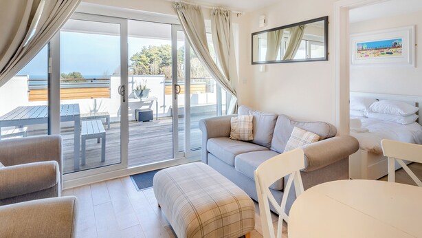 A modern room with a sofa, a dining table, and a balcony with a view. - 2 bedroom accommodation in Brixham (Brixham)