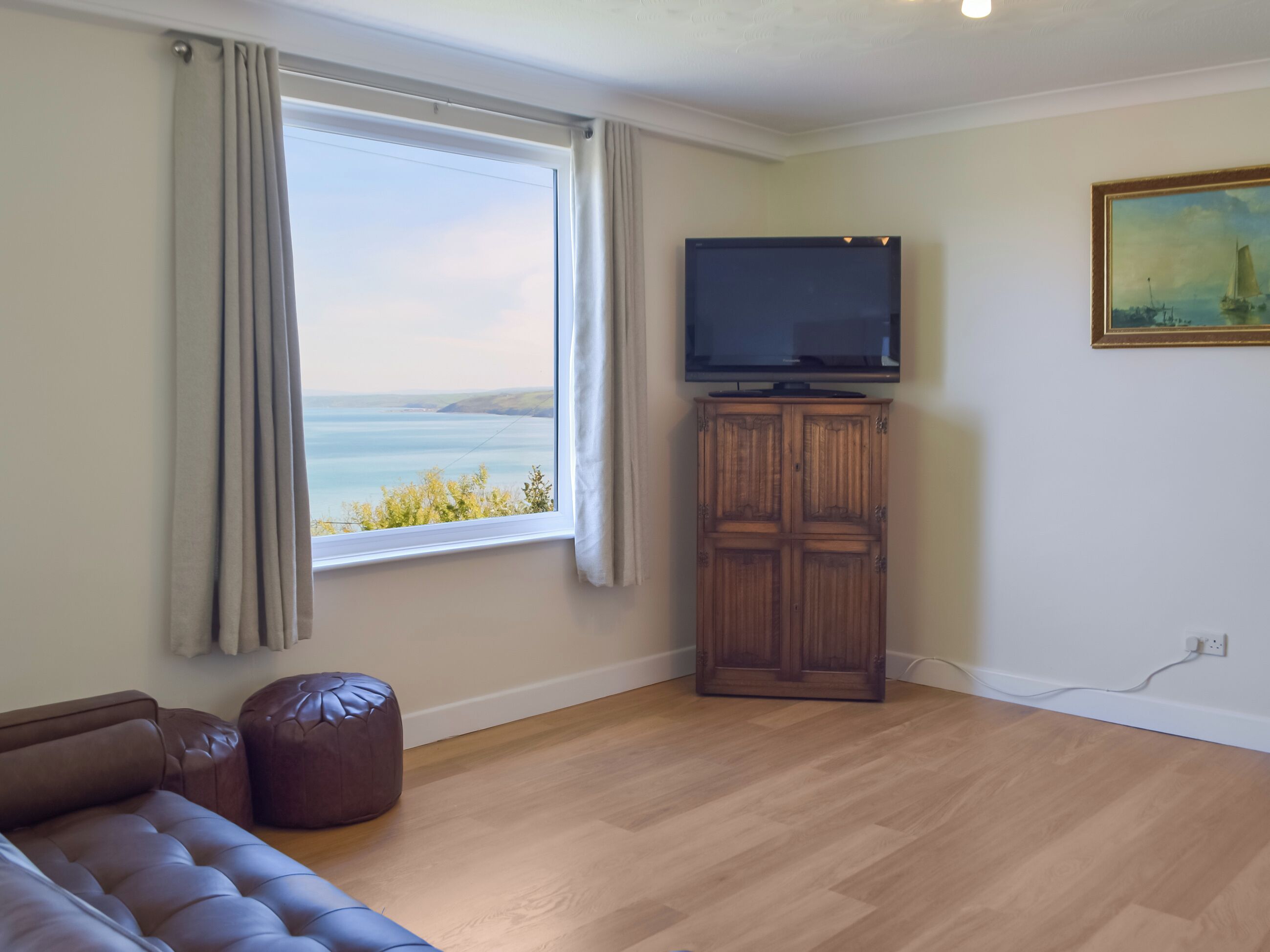 A living room with a large window, a flat-screen TV, a wooden cabinet, and a brown leather sofa.