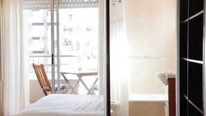A bedroom with a bed, a wooden chair, a balcony with a view of buildings, and a bathroom with a sink and toilet. - Beautiful apartment in Palermo Soho (Buenos Aires)
