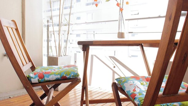 A wooden deck with two chairs and a table, a potted plant, and a view of a building. - Beautiful apartment in Palermo Soho (Buenos Aires)