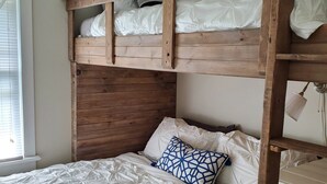 A bunk bed with a wooden frame, white bedding, and a blue patterned pillow.