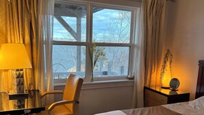 A hotel room with a bed, a desk with a lamp, a chair, and a window with a view of trees and a building. - Luxury retreat with Amazing Views, Great Location with free parking! (Halifax)