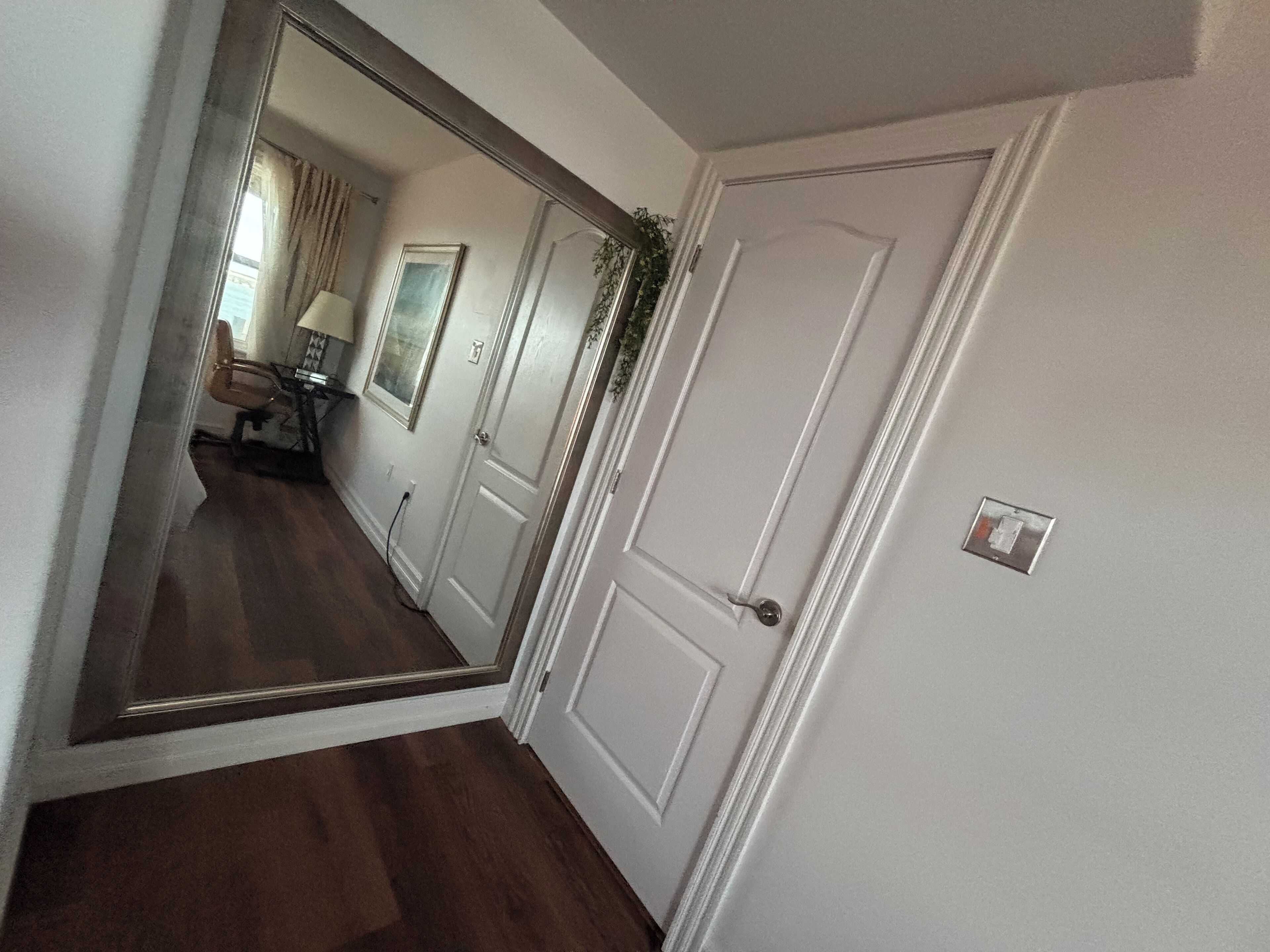 A hallway with a wooden floor, white walls, and a door with a small window.