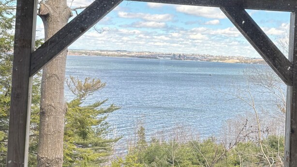 A view through a window with a wooden frame, overlooking a body of water and a distant shoreline with buildings. - Luxury retreat with Amazing Views, Great Location with free parking! (Halifax)