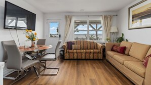 A modern living room with a sofa, a dining table with chairs, a TV mounted on the wall, and a large window with curtains. - Luxury retreat with Amazing Views, Great Location with free parking! (Halifax)