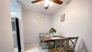 A dining area with a wooden table and chairs, a ceiling fan, and a refrigerator in the background.