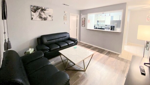 A living room with a black leather sofa, a coffee table, and a painting on the wall.