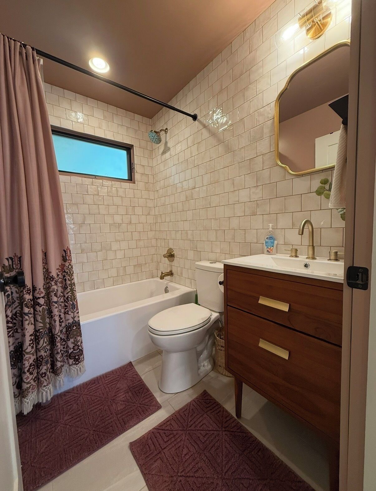 A bathroom with a bathtub, toilet, vanity with a mirror, and patterned curtains.