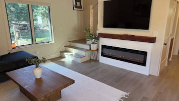 A modern living room with a fireplace, a flat-screen TV, and a staircase leading to another level.