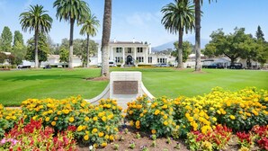 A building with a central entrance, surrounded by a well-maintained lawn and a variety of flowering plants.