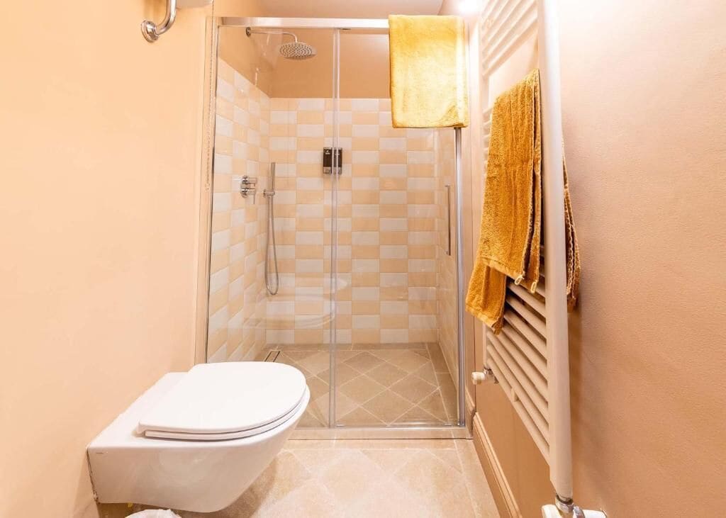 Une salle de bain avec une douche à parois de verre, des toilettes blanches et un porte-serviettes avec une serviette jaune.
