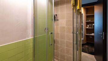 A bathroom with a glass shower enclosure, a green-tiled wall, and a beige-tiled floor.