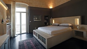 Un dormitorio con cama, mesitas de noche, una ventana con cortinas y una puerta.