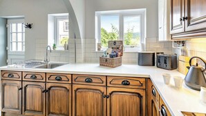Une cuisine dotée d’un grand îlot central, de meubles en bois, d’un évier et d’une fenêtre donnant sur un paysage verdoyant.
