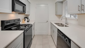 A compact kitchen with white cabinets, a black stove, a microwave, and a sink.
