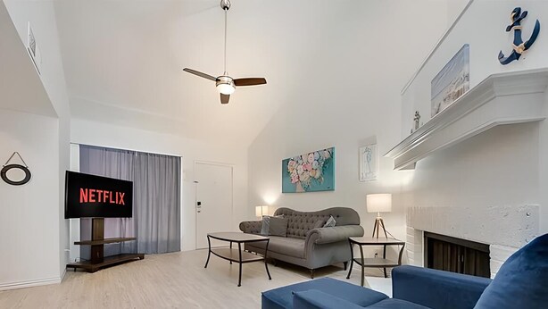 A modern living room with a flat-screen TV, a grey sofa, a blue armchair, and a fireplace.