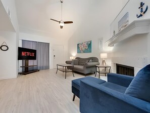 Un salon moderne avec un téléviseur à écran plat, un canapé gris, un fauteuil bleu et une cheminée.