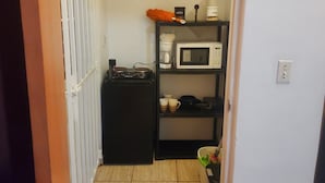 A small kitchen with a microwave, coffee maker, and shelves with kitchenware.