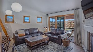 A spacious living room with two leather sofas, a wooden coffee table, and a large window offering a view of a mountainous landscape.