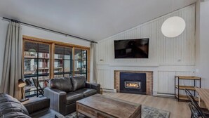 A modern living room with a fireplace, leather sofa, and a large TV mounted on the wall.