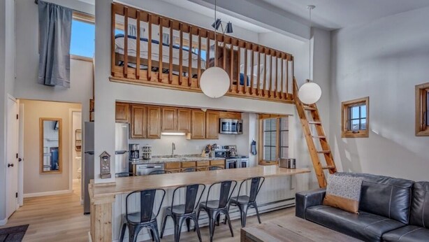 A spacious living area with a high ceiling, a wooden staircase, and a kitchen with modern appliances.