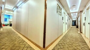 A hotel corridor with a patterned carpet, recessed lighting, and a central column with a decorative element. - Shanghai Nalan Hotel (Shanghai)