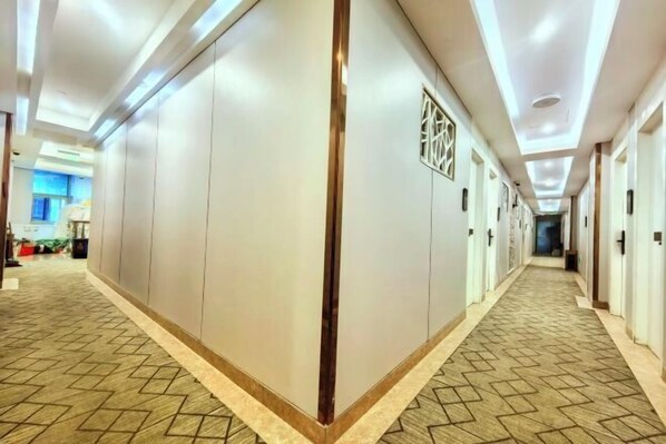 A hotel corridor with a patterned carpet, recessed lighting, and a central column with a decorative element. - Shanghai Nalan Hotel (Shanghai)