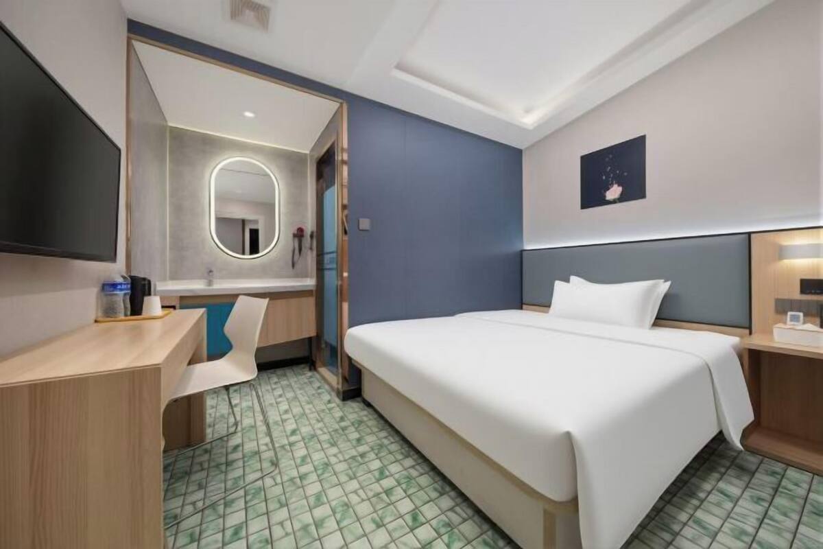 A hotel room with a bed, a desk, a chair, a mirror, and a TV.