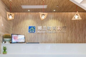 A reception desk with a wooden wall background, a logo, and a sign for Nalan Fashion Hotel. - Shanghai Nalan Hotel (Shanghai)