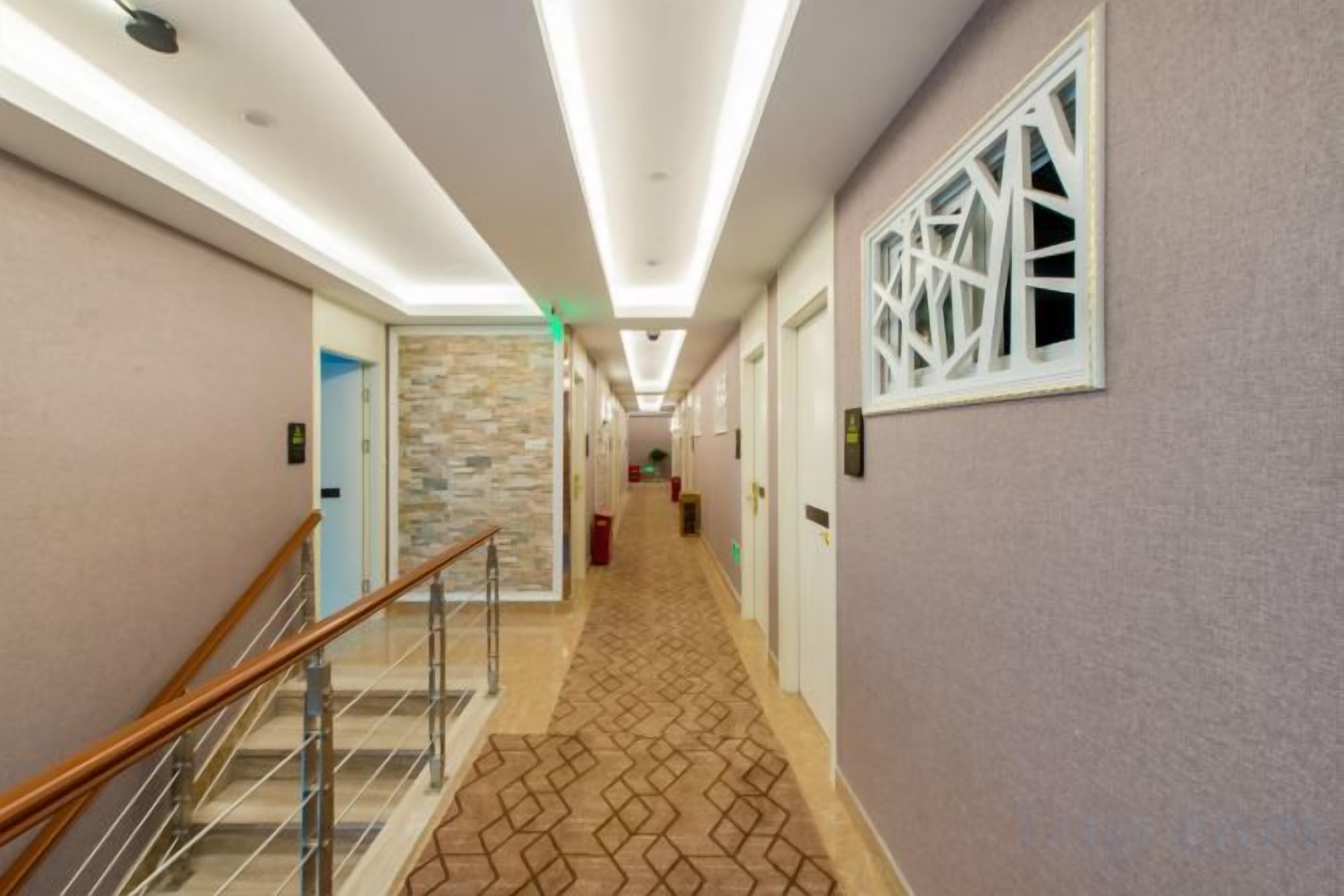 A hotel hallway with a patterned carpet, a staircase with a metal railing, and a stone accent wall.