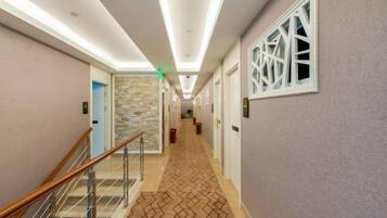 A hotel hallway with a patterned carpet, a staircase with a metal railing, and a stone accent wall.