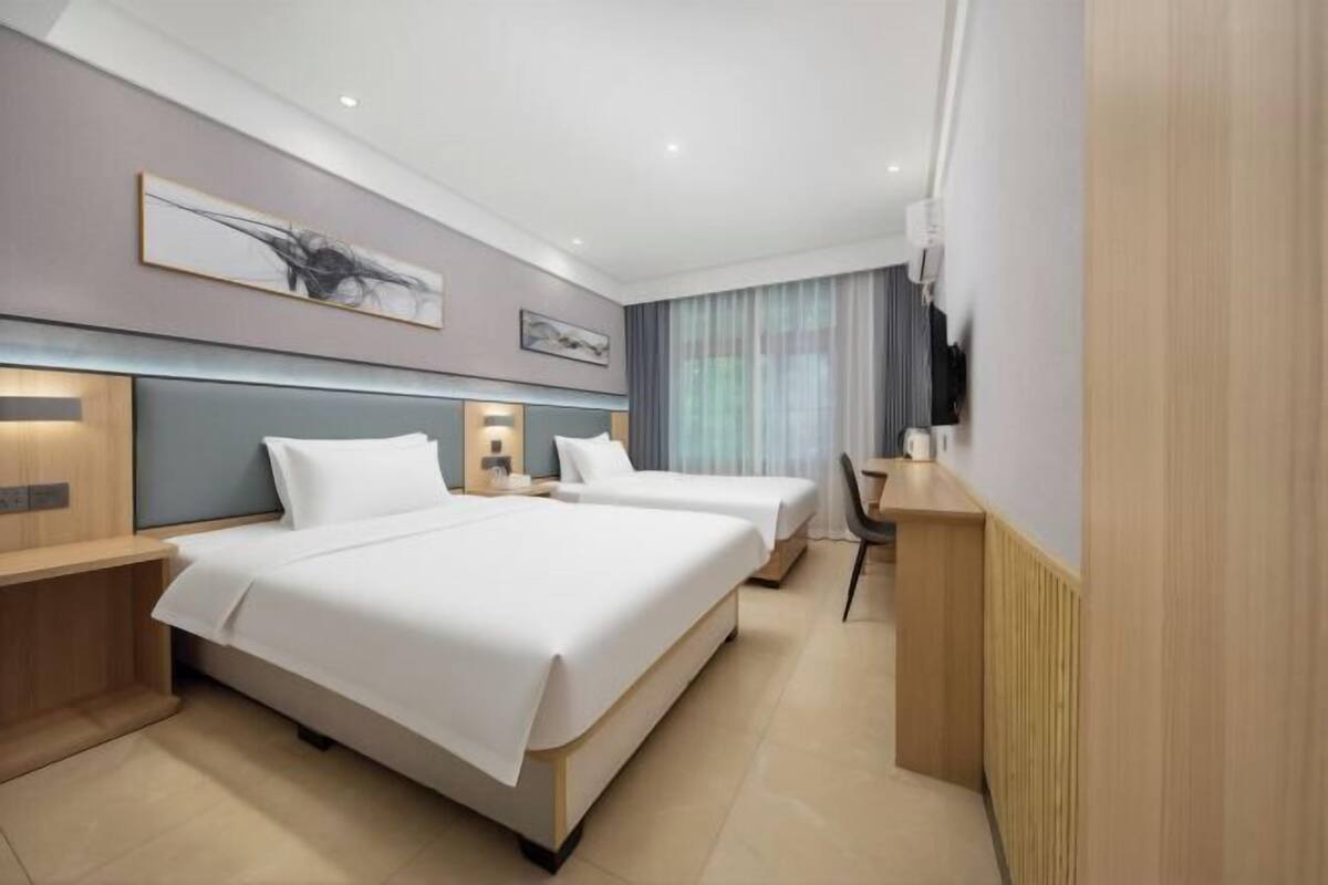 A hotel room with two beds, a desk, a chair, and a TV.