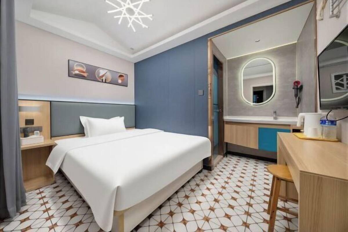 A hotel room with a bed, bedside table, mirror, and a small desk with a chair.
