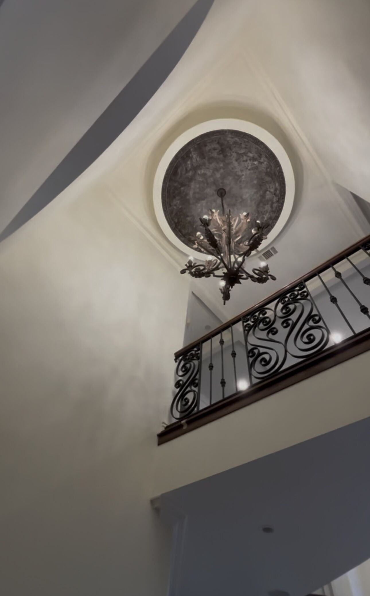 A grand staircase with a decorative iron railing and a round, textured ceiling.
